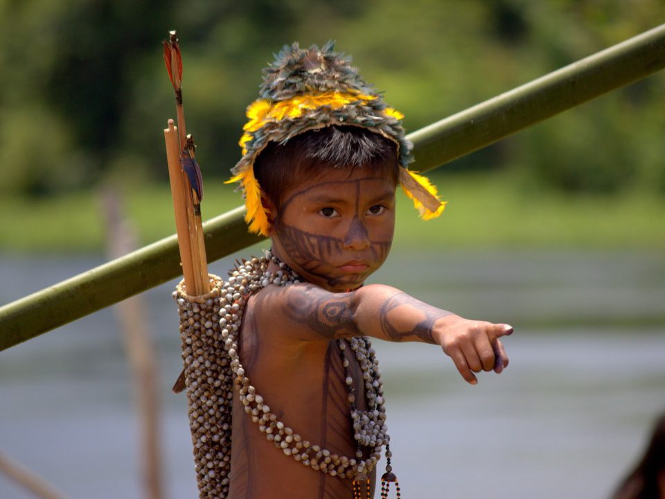 Ein Munduruku-Knabe in traditioneller Kleidung zeigt mit dem Finger in die Ferne.