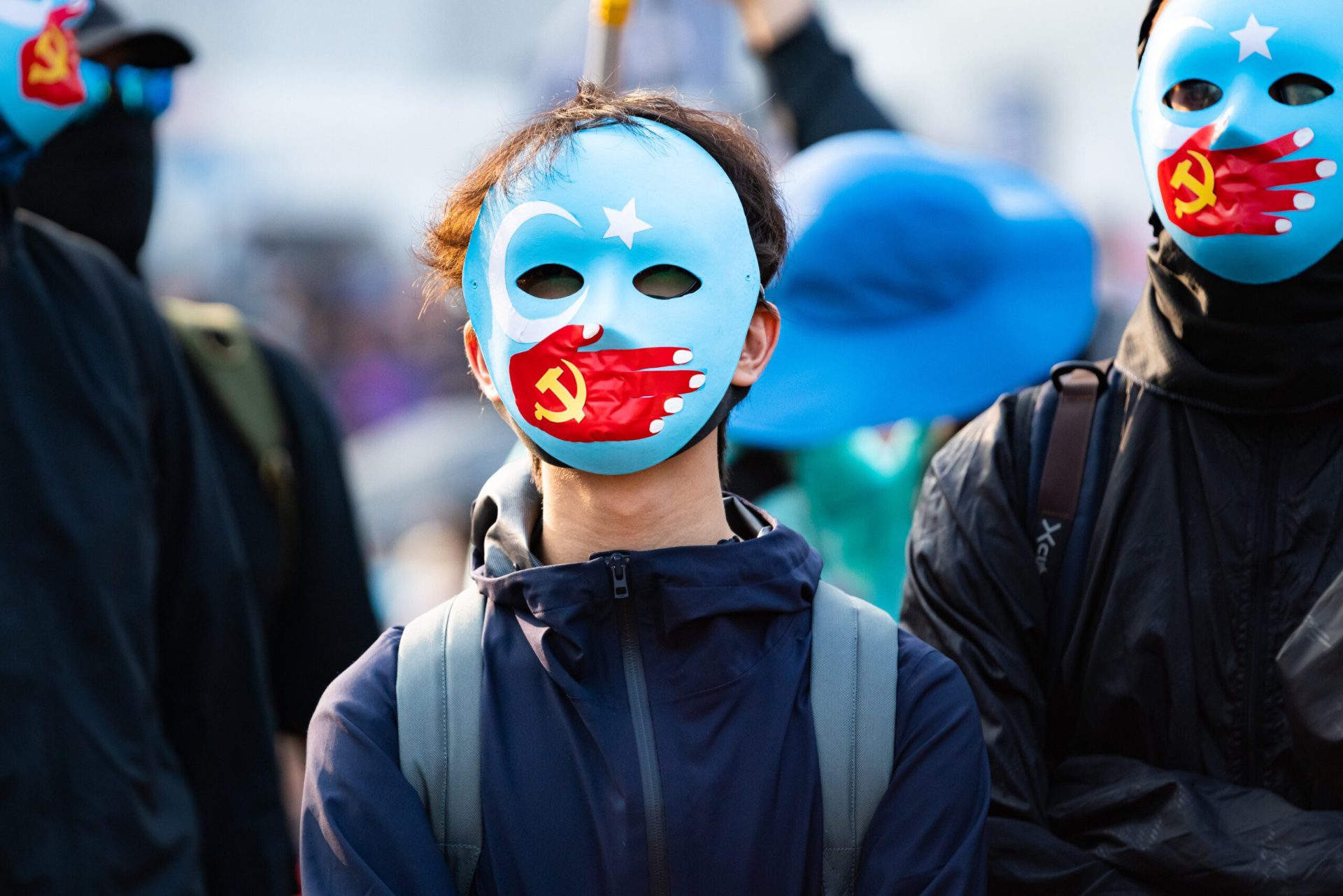 Uigurische Demonstrierende mit Masken, auf denen eine rote Hand über dem Mund liegt, als Symbol für Chinas Repressionen.